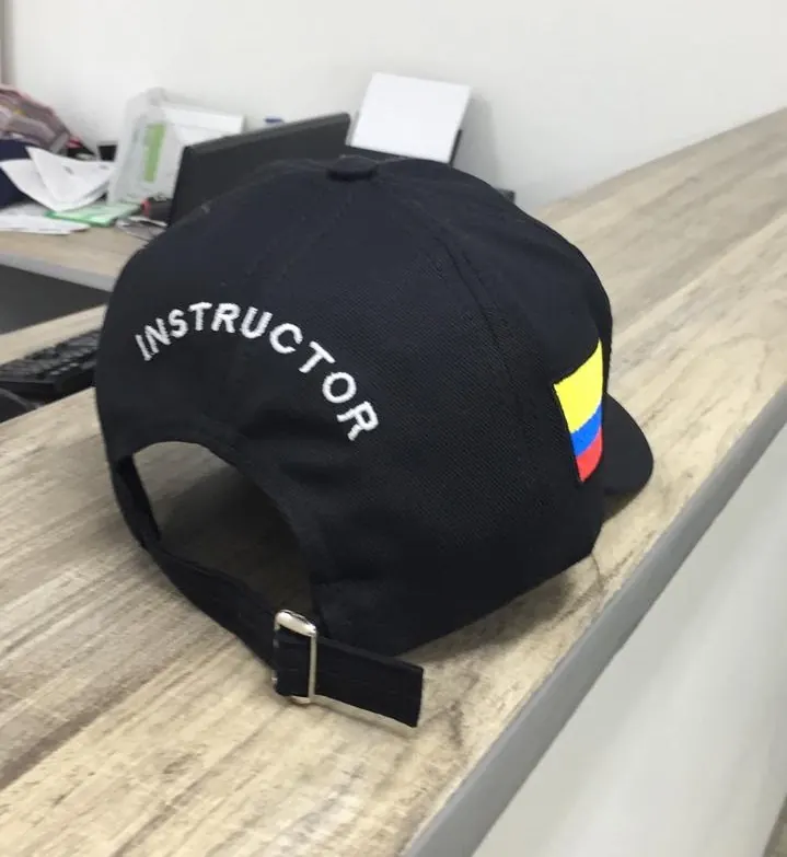Parte posterior de gorra negra con palabra Instructor y bandera de Colombia bordadas
